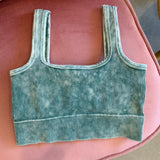 A ribbed knit crop top in a washed teal green color, laid flat on a pink upholstered chair.