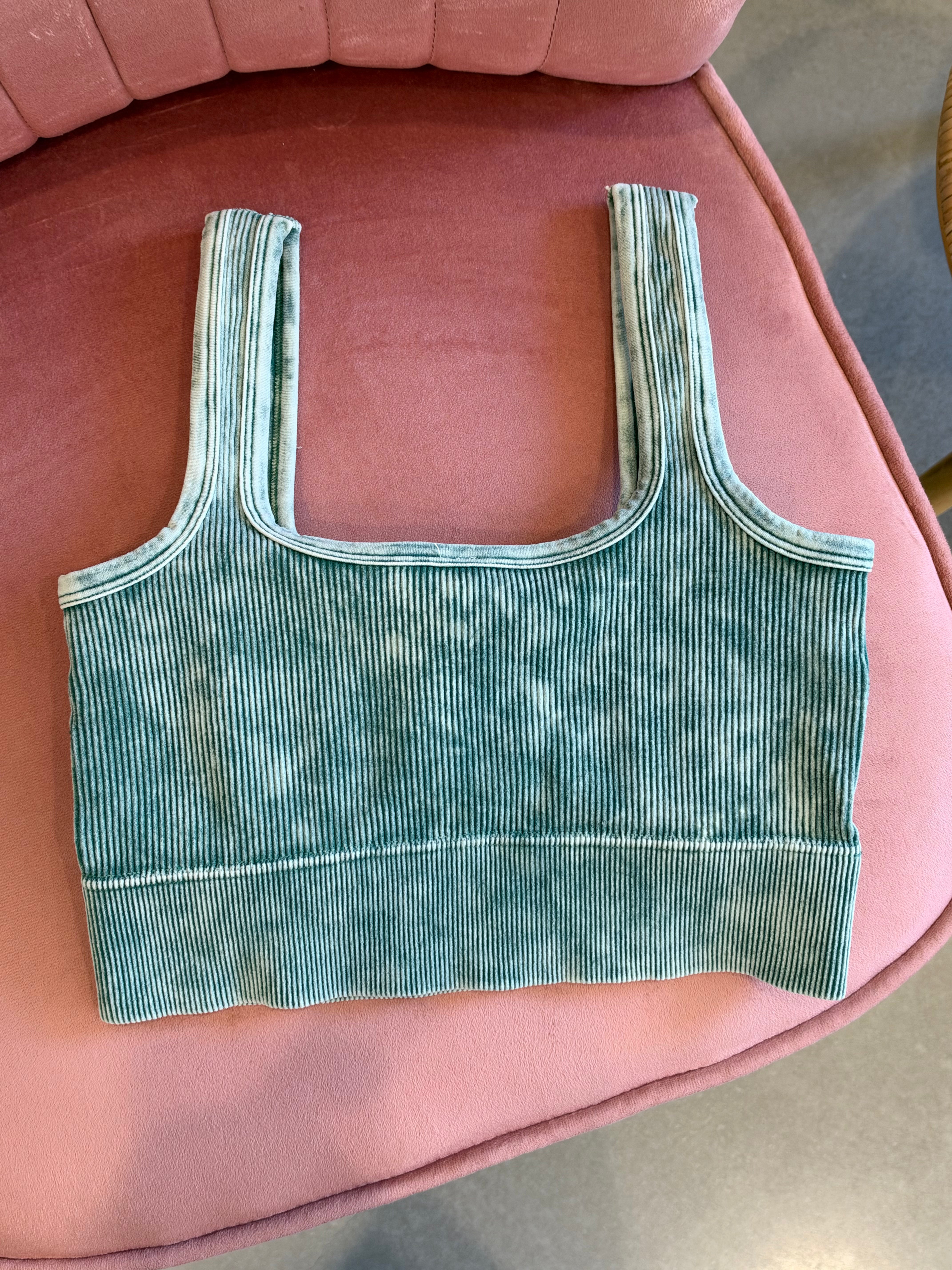 A ribbed knit crop top in a washed teal green color, laid flat on a pink upholstered chair.