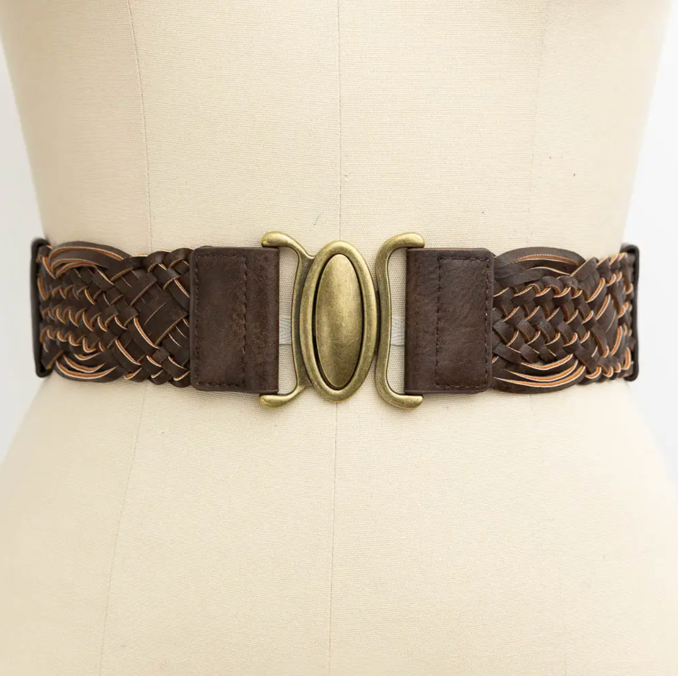 A dark brown braided leather belt with a central brass oval buckle, displayed on a cream-colored dress form.