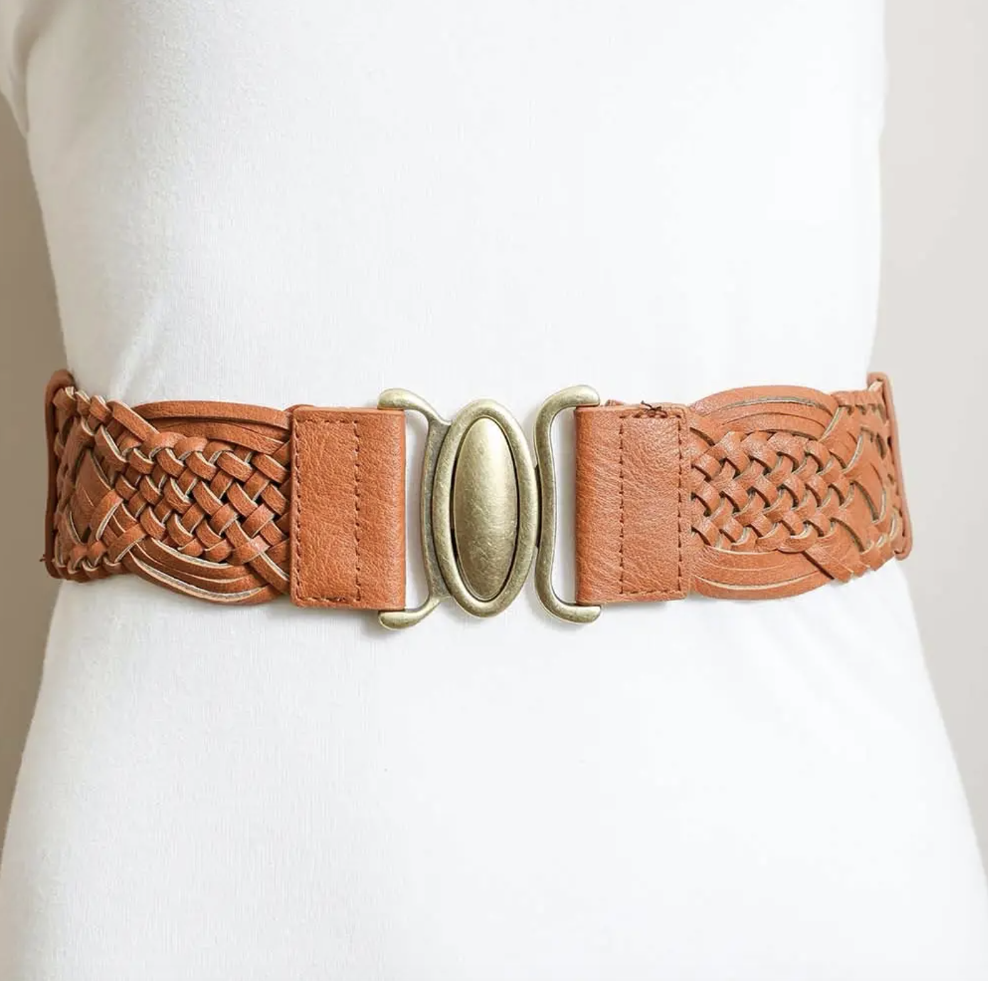 A tan leather belt with braided detailing and a gold-toned oval buckle, shown worn on a white dress form.
