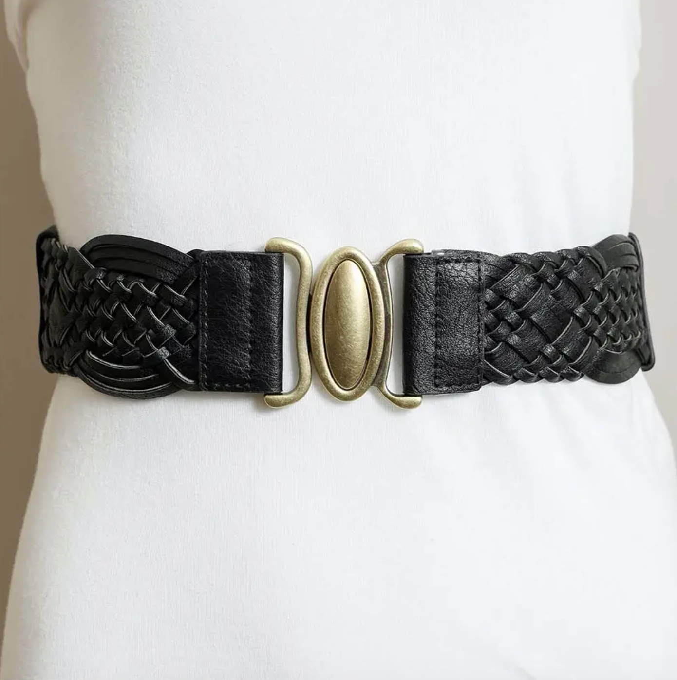 A black braided leather belt with a central antique gold oval buckle, displayed on a white mannequin torso.