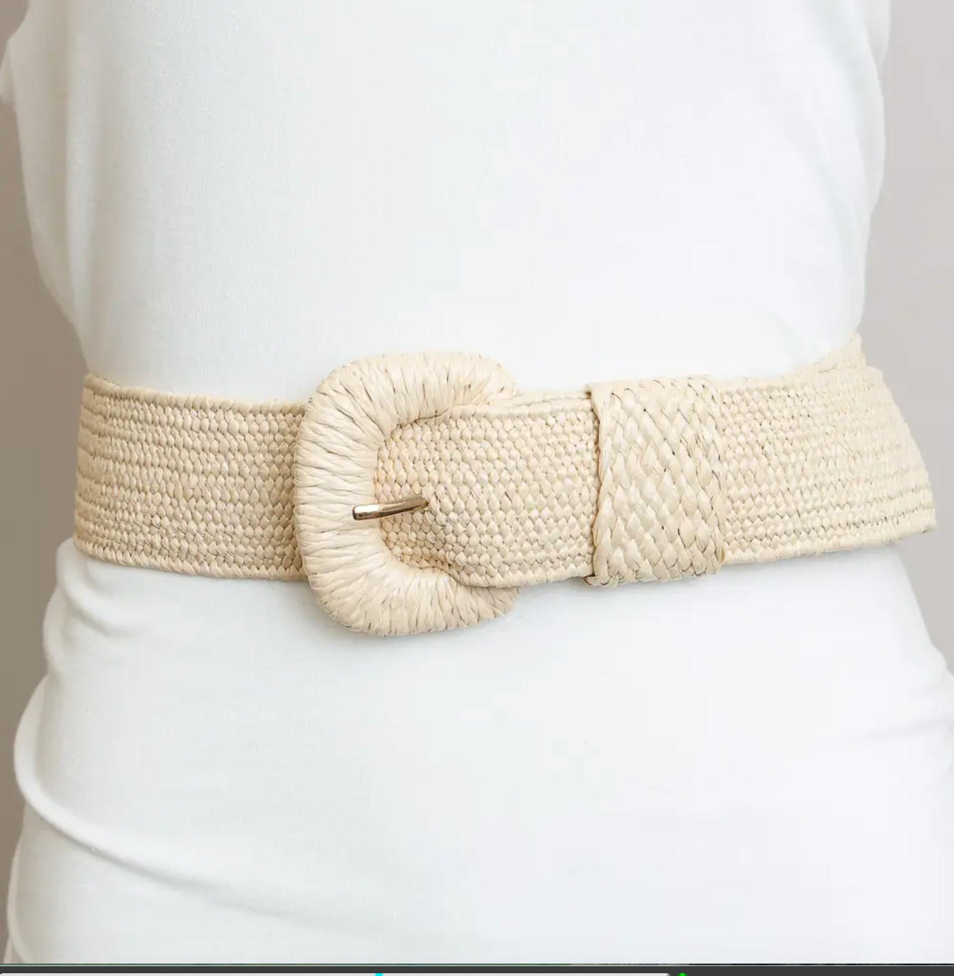 A wide, woven beige belt with a large round buckle, worn over a white top.