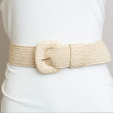 A wide, woven beige belt with a large round buckle, worn over a white top.