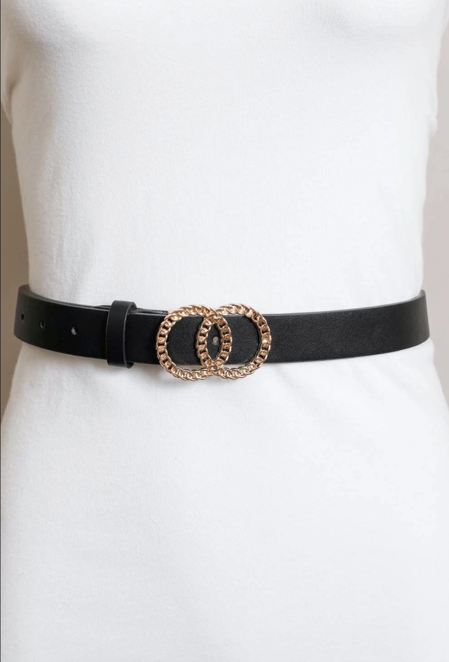 A black faux-leather belt with a double interlocking oval buckle in a gold-tone finish, displayed on a white mannequin torso.