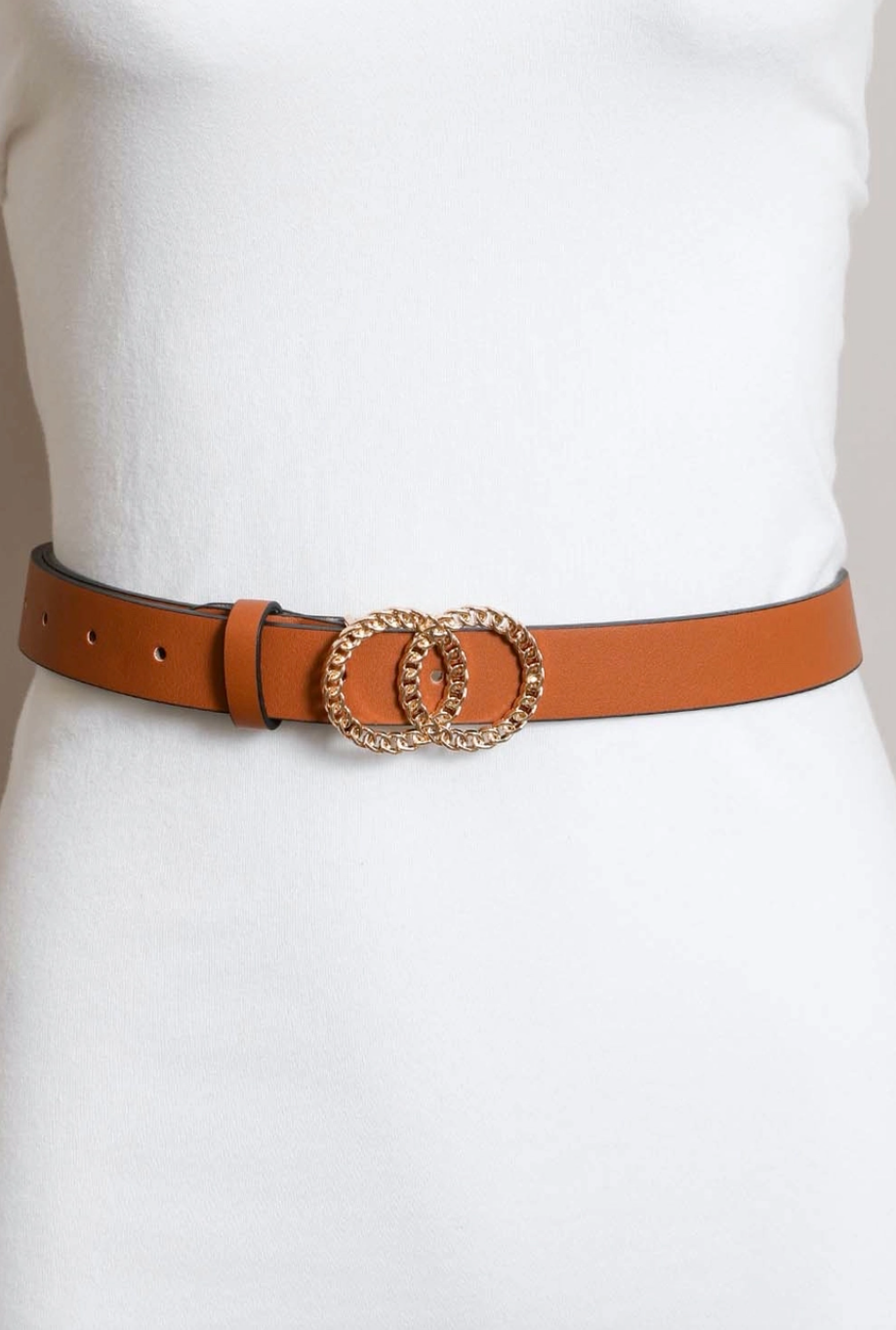 A slim tan leather belt with a double interlocking oval buckle embellished with gold-toned crystals, shown worn on a white mannequin torso.