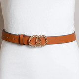 A slim tan leather belt with a double interlocking oval buckle embellished with gold-toned crystals, shown worn on a white mannequin torso.